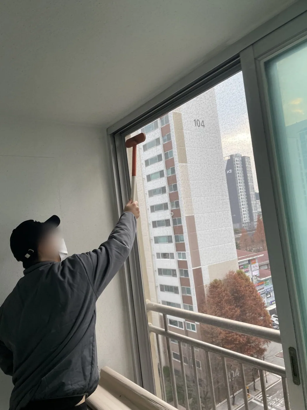 작업자가 스퀴지로 베란다 창의 상부 유리를 위에서 아래로 밀어내는 장면