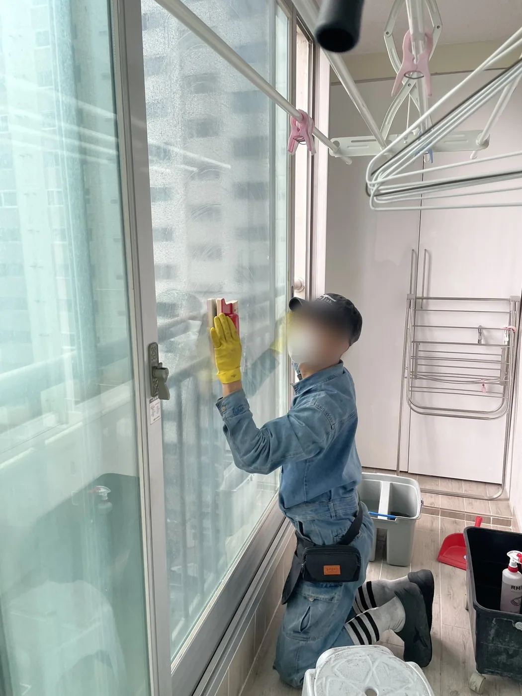 작업자가 무릎을 굽히고 베란다 창 하부 유리를 손으로 닦는 장면
