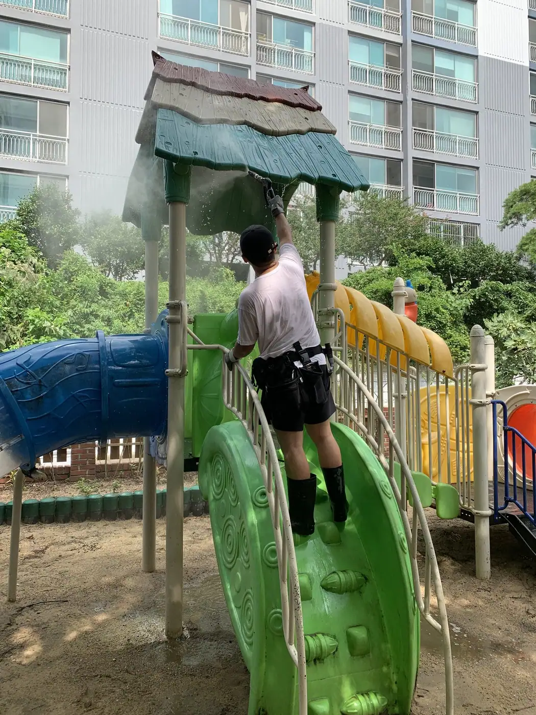 놀이대 상판에 올라서서 지붕 쪽을 세척하는 장면