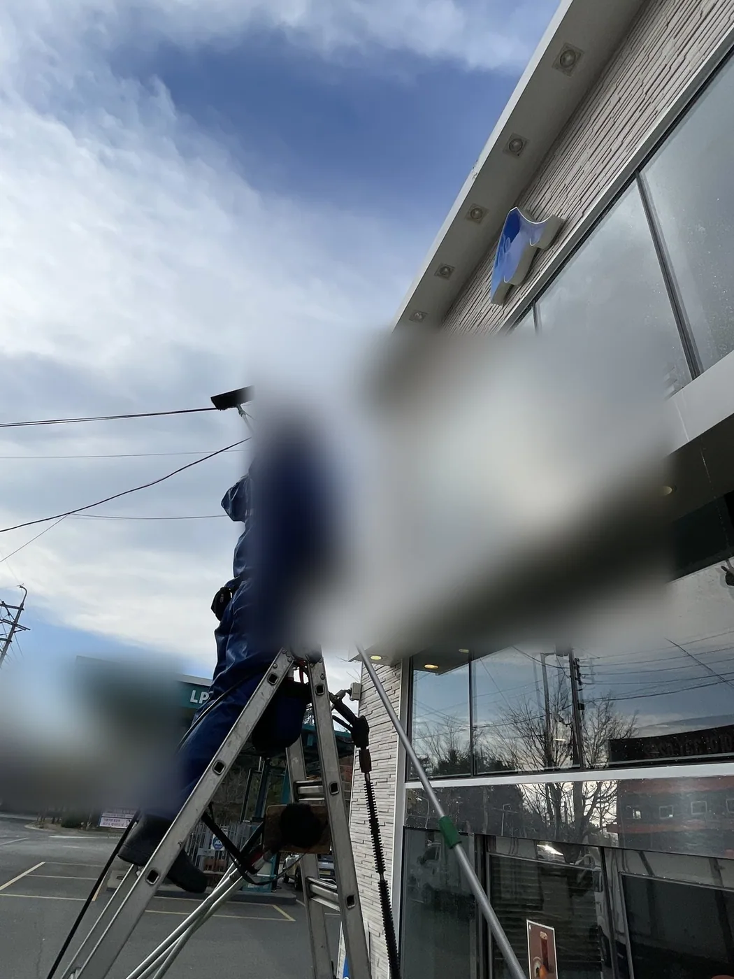 사다리 위 작업자가 벽면과 유리가 만나는 구간을 폴대 도구로 세척하는 장면