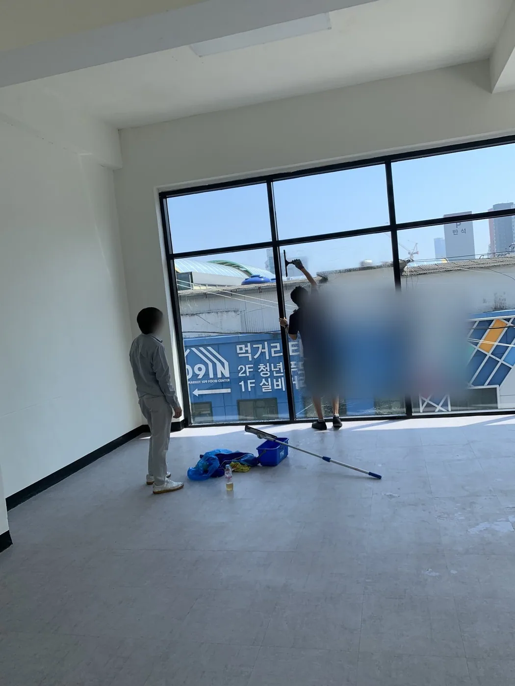 두 작업자가 유리면의 상부와 하부를 나눠 마무리하는 장면