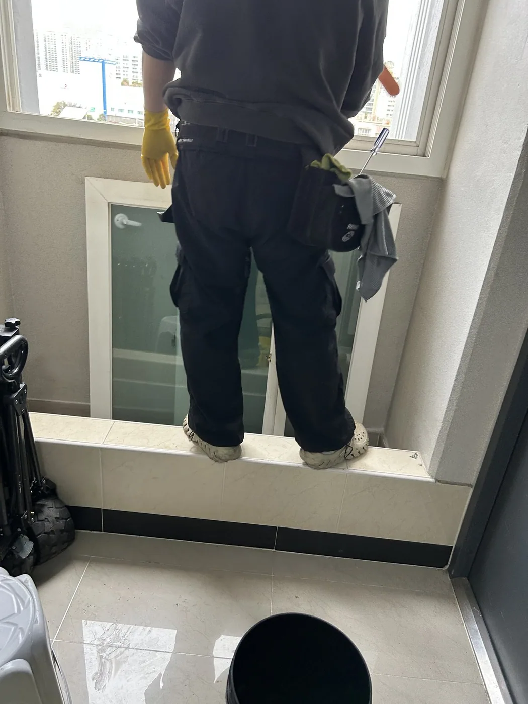 작업자가 창턱에 올라서서 창의 상부 유리면을 닦는 장면